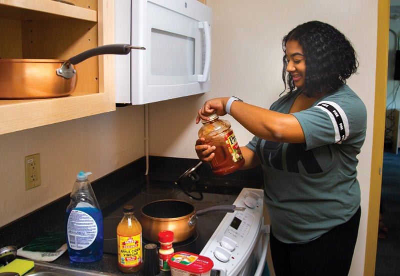 Riley Hall features laundry facilities, private courtyard, study and lounge spaces, and more. Photo of resident using kitchenette in Riley Hall